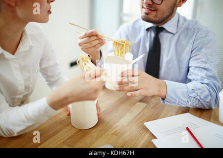 Deux jeunes financiers eating chinese wok à partir de boîtes de papier par lieu de travail et avoir parler Banque D'Images