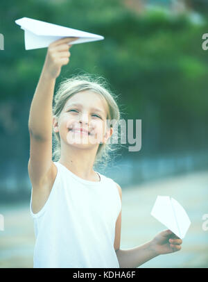 Smiling girl in elementary school age jouant avec le vol des avions en papier en plein air Banque D'Images