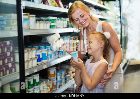 Une femme heureuse et cute smiling girl picking produits laitiers frais dans la section réfrigérée dans l'épicerie Banque D'Images