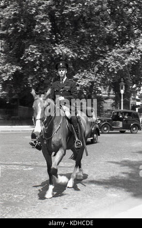 Années 1950, Londres, Westminster, photo historique d'un policier britannique monté à cheval, avec un taxi londonien de l'époque en arrière-plan. Notez la zone en plein air dans le taxi à côté du conducteur, un espace pour mettre des bagages. Banque D'Images