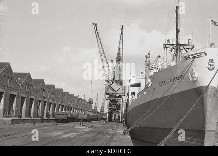 Années 1960, historique, le bateau à conteneurs, City of Oxford, amarré à London Docks, Londres, Angleterre, Royaume-Uni. Sur l'image sont les wagons de fret ferroviaire à côté des dépôts de stockage. Construit en 1948 à Glasgow sur le Clyde par John Brown & Co pour Ellerman Lines, le cargo était alimenté à la vapeur et a survécu jusqu'en 1978 quand il a été cassé. Banque D'Images