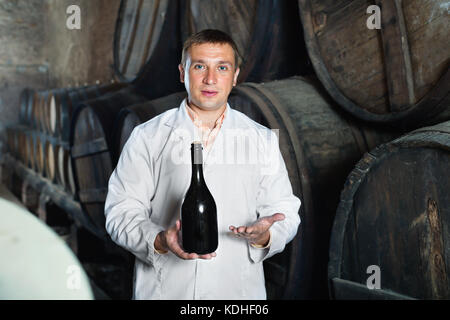 Wine house technician holding bouteille près de fûts de bois dans le stockage Banque D'Images