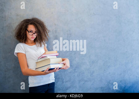 Portrait of teenage girl avec des lunettes se dresse à côté du mur et détient plusieurs livres Banque D'Images