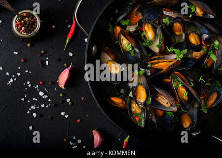 Les moules dans une sauce au vin avec des herbes dans une poêle sur un fond noir. Télévision. vue d'en haut. Banque D'Images