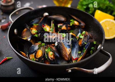 Les moules dans une sauce au vin avec des herbes dans une poêle sur un fond noir. Banque D'Images