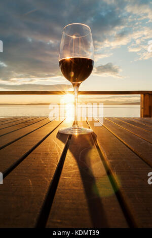 Hero verre de vin rouge sur la table à lattes au coucher du soleil par la mer Banque D'Images