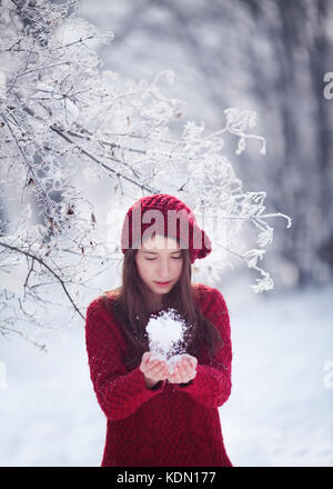 Girl in red knitting porter la tenue de la neige dans ses mains, scène d'hiver Banque D'Images