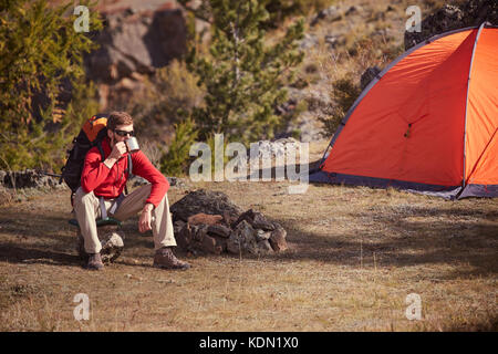 Backpacker ayant reste près d'orange, thé boissons tente à partir de la tasse . Banque D'Images