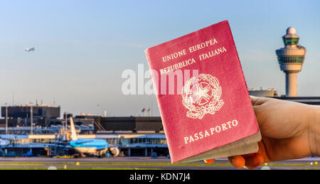 Digital composite de main tenant un passeport italien avec terminal de l'aéroport occupé en arrière-plan flou Banque D'Images