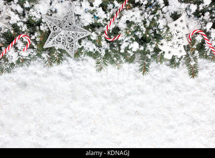 Fond de noël avec sapin de noël décoré avec des cannes de bonbon, ornements et flocons de neige sur une épaisse couche de neige irisée. Banque D'Images