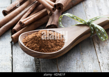 Close up de cuillère en bois remplis de cannelle en face de bâtons de cannelle. Banque D'Images