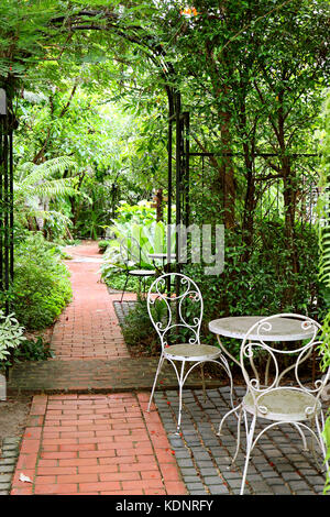 Photo verticale de table en fer forgé blanc et des chaises dans le jardin avec allée pavée de briques Banque D'Images