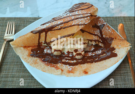 La crêpe à la banane et sauce au chocolat servi sur plaque blanche Banque D'Images