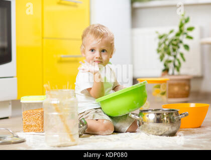 Bébé garçon enfant assis sur le plancher de la cuisine et jouer avec la farine. Banque D'Images