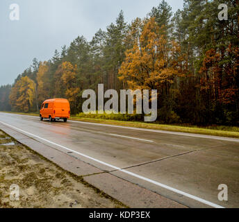 Voiture orange-van, passe le long de la route d'automne au coucher du soleil. La voiture est en mouvement dans la soirée. de beaux paysages aux couleurs jaune-orangé et forêt o Banque D'Images