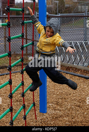 Un petit garçon (5 ans) d'un saut d'une escalade dans un parc. Banque D'Images