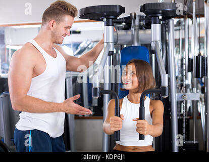 Homme bien formé d'aider l'entraîneur jeune femme en utilisant des machines à l'intérieur de sport pont pec Banque D'Images