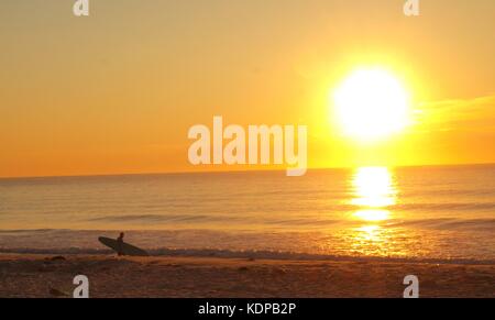 Un lever de soleil sur la côte du New Jersey à Ocean Beach en tant que surfer attend la fin de la vague parfaite. Banque D'Images