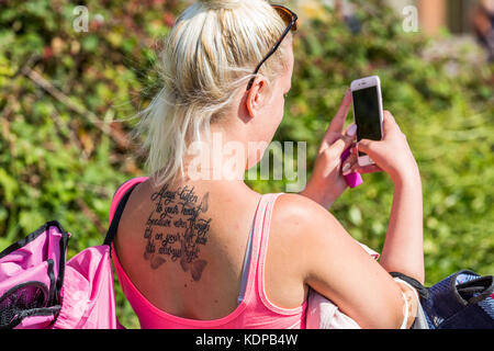 Une jeune femme aux cheveux blonds portant un coupe-bas haut et des lunettes avec un tatouage sur son dos en tenant une photo de selfies, Bournemouth, England UK Banque D'Images