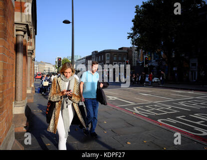 Caucasian woman wearing manteau en fausse fourrure à la recherche à son smartphone en marchant sur la chaussée à Londres, Angleterre Banque D'Images