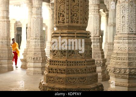 Un moine dans une robe orange marche parmi des colonnes dans le temple Ranakpur Jain au Rajasthan, Inde Banque D'Images