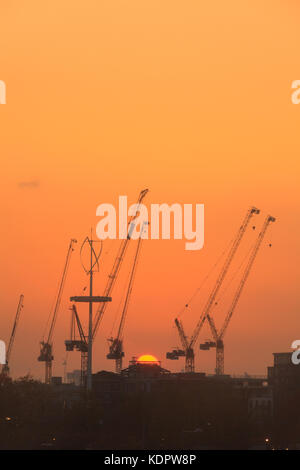 Un beau soleil orange se couche derrière les nombreuses grues de construction à Stratford's regeneration zone autour du Queen Elizabeth Olympic Park, sur un accueil chaleureux et très ensoleillé jour fin octobre dans l'Est de Londres. Banque D'Images