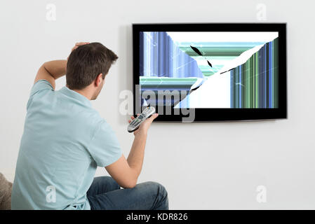 Homme frustré assis sur un canapé en face de la télévision montrant l'écran déformé Banque D'Images