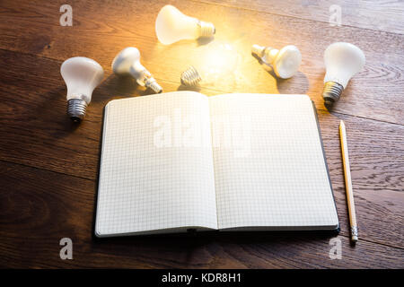 Vue en grand angle d'un carnet ouvert avec ampoules lumineuses et crayon sur un bureau en bois Banque D'Images