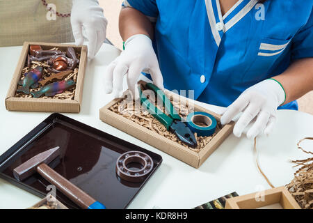 Une femme en uniforme bleu confiseur est boîtes d'emballage de bonbons de chocolat sous la forme d'outils : pinces, marteau, Scotch et autres outils Banque D'Images