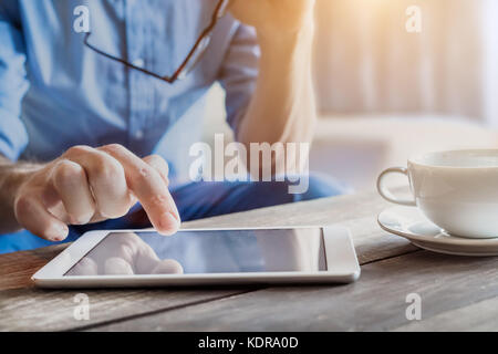 Young businessman using digital tablet ordinateur sur une table en bois avec une tasse de café, homme de main de toucher l'écran, arrière-plan flou Banque D'Images