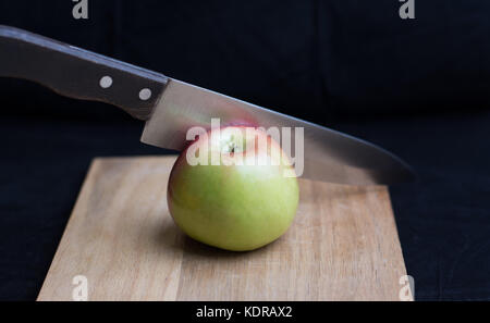 Un couteau tranchant un miel-crisp apple sur une planche à découper. Banque D'Images