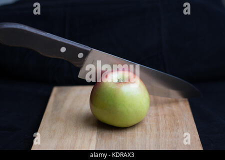 Un couteau tranchant un miel-crisp apple sur une planche à découper. Banque D'Images