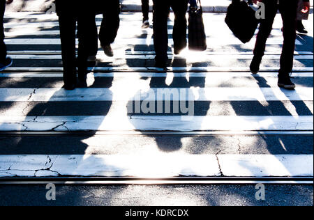 Zebra crossing floue avec silhouettes et ombres de personnes à pied dans le froid et ensoleillé tôt le matin, jour d'automne en noir et blanc Banque D'Images