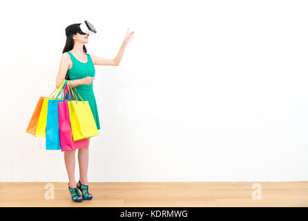 Belle jeune femme shopper debout sur un plancher en bois avec des sacs colorés et portant l'équipement casque vr faire de geste d'appui à la recherche Banque D'Images