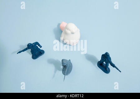 Troupe de soldats de plomb en plastique protégeant un mignon petit oiseau en céramique sur un fond bleu. couleur minimal still life photography Banque D'Images