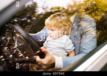 L'homme conduisant une voiture avec peu de fils. tout-petit garçon dans ses pères tour. Tourné à travers le verre. Banque D'Images