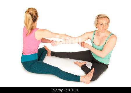 Charges latérales élevées sur tout le corps de deux jeunes femmes blonde assise sur le sol de toucher la plante des pieds et tenir la main pendant un partenaire yoga Banque D'Images
