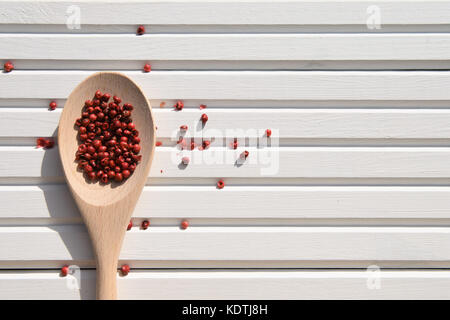 La photographie alimentaire image de nouveau cuillère en bois avec poivre rouge rose saupoudré sur fond de bois blanc de soleil pris sur la côte sud de l'Angleterre Banque D'Images