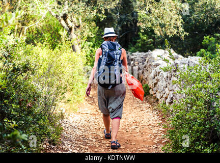 Sentier de randonnée femme on country rock avec clôture et bois. randonneur avec un chapeau est le trekking à travers la jungle de l'île sur terrain rugueux silba croatie. Banque D'Images