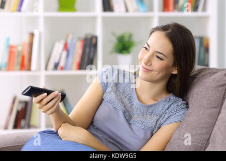 Femme regardant la télévision holding remote control assis sur un canapé à la maison Banque D'Images