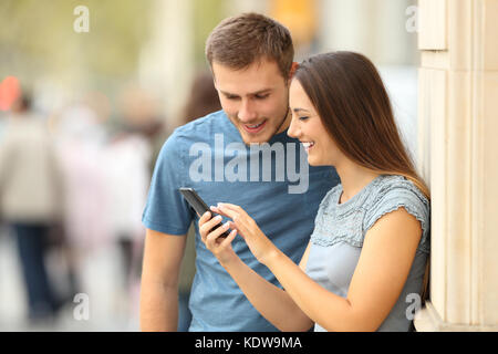 Happy casual couple contrôle de contenu dans un téléphone intelligent debout sur la rue Banque D'Images
