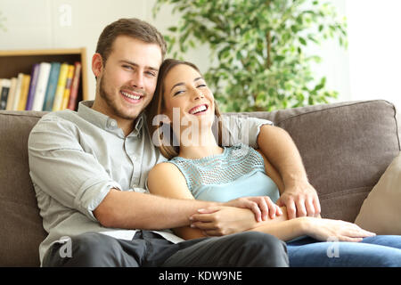 Heureux couple hugging and posing looking at camera assis sur un canapé à la maison Banque D'Images