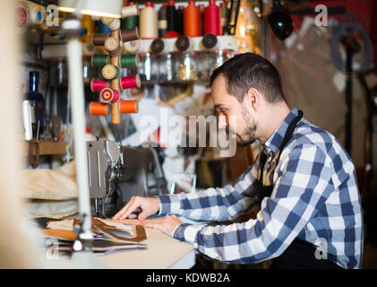 Smiling american travailleur homme points de couture sur ceinturon en cuir atelier Banque D'Images