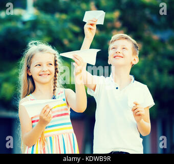 Deux heureux enfants jouant avec des avions en papier dans la ville le jour de l'été Banque D'Images
