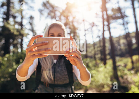 Female hiker en regardant son téléphone portable en le tenant à deux mains. Trekker femme prendre aide de téléphone mobile pour la navigation en forêt. Banque D'Images