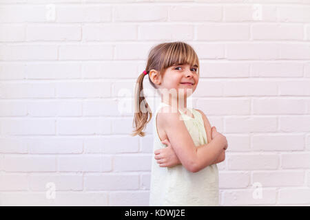 Jolie petite fille blonde profil enfant portrait demi-longueur. Cute kid avec bras croisés contre le mur en brique blanche Banque D'Images