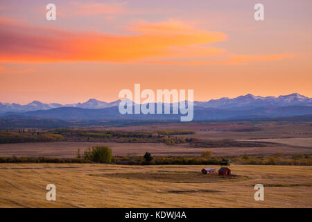 Les nuages captent le coucher de soleil au-dessus des contreforts à l'ouest de Calgary où les champs sont récoltés. Banque D'Images