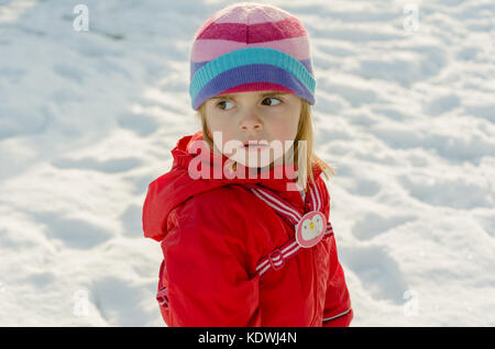 Jolie petite fille d'âge préscolaire en hiver neige scène portant des habits rouges et stripy woolly hat pendant les vacances Banque D'Images