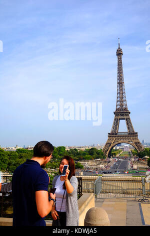 Un jeune couple montrant l'un à l'autre les autoportraits qu'ils ont prises sur leurs smartphones avec la Tour Eiffel à Paris dans l'arrière-plan Banque D'Images