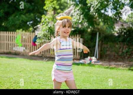 Jolie petite fille d'âge élémentaire sur l'équilibrage de la journée des sports de sac d'haricot jaune sur la tête. happy fun concept retour à l'école. Banque D'Images